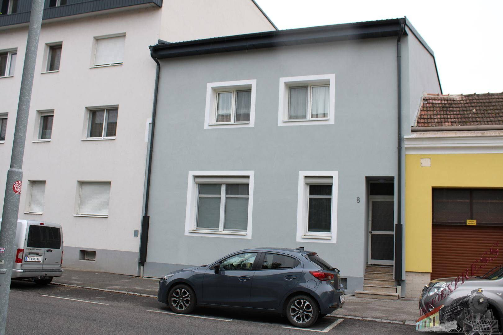 Vorderansicht eines modernen Reihenhauses mit grauer Fassade und weißen Fenstern an der Straße.