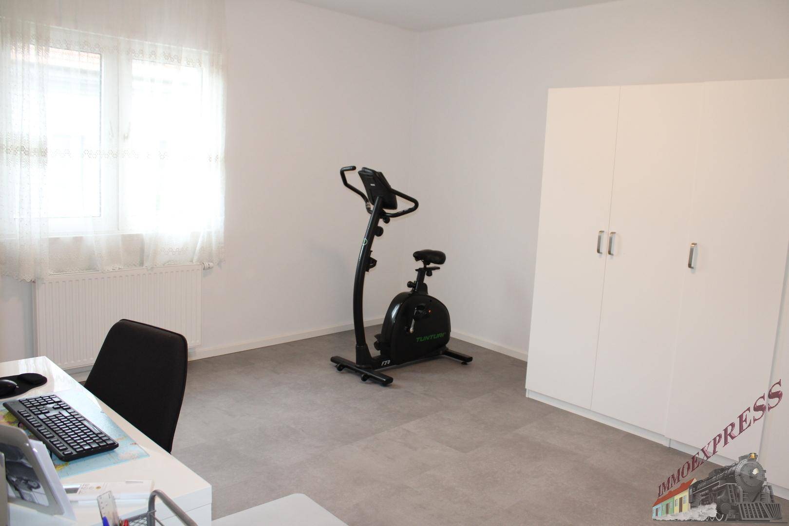 Helles Arbeitszimmer mit Schreibtisch, Bürostuhl und einem Heimtrainer für sportliche Aktivitäten.