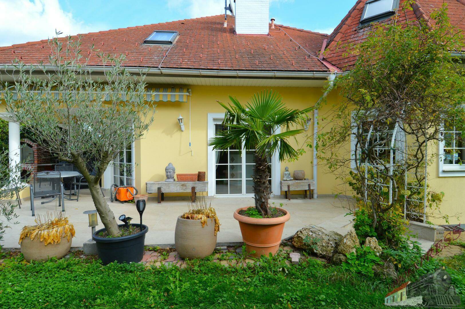Sonnenterrasse mit Pflanzenkübeln, Gartenbereich und Blick auf das Haus.