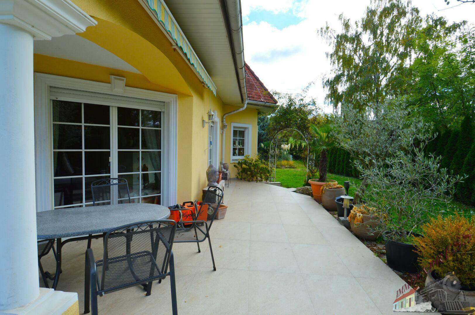 Große Terrasse mit Gartenmöbeln, Markise und Zugang zum Garten.