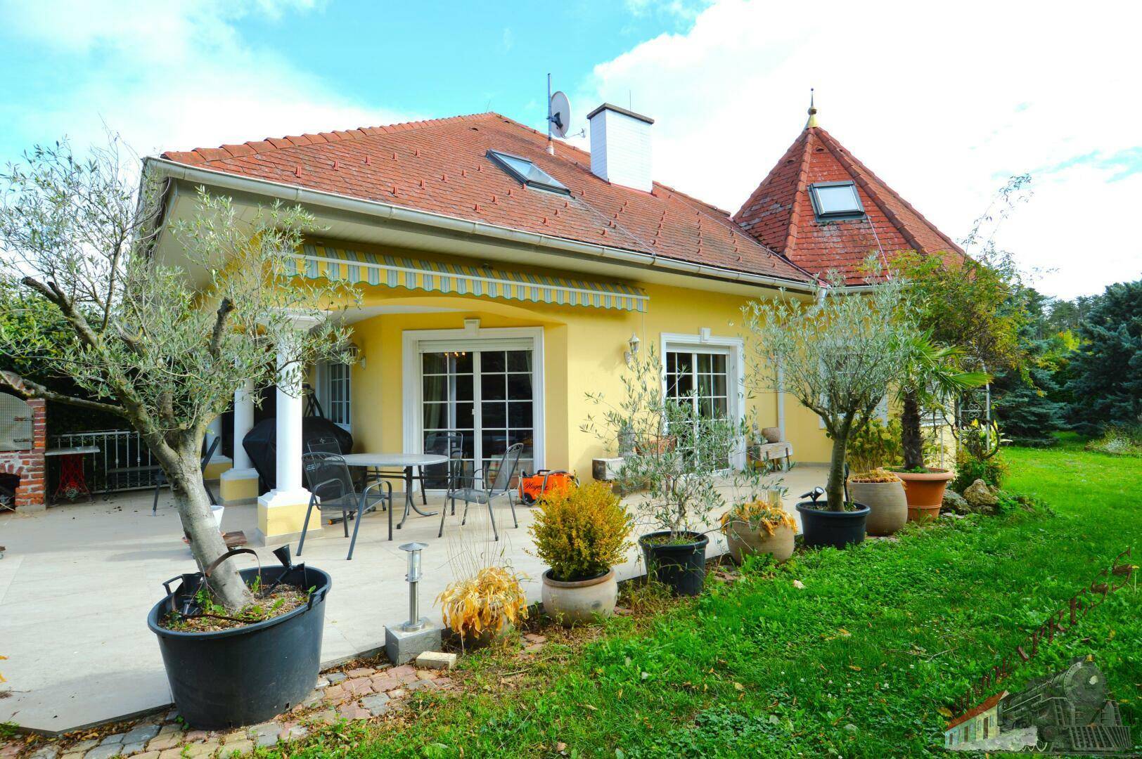 Weitläufige Terrasse mit Gartenmöbeln, Rasenfläche und mediterranen Pflanzen.