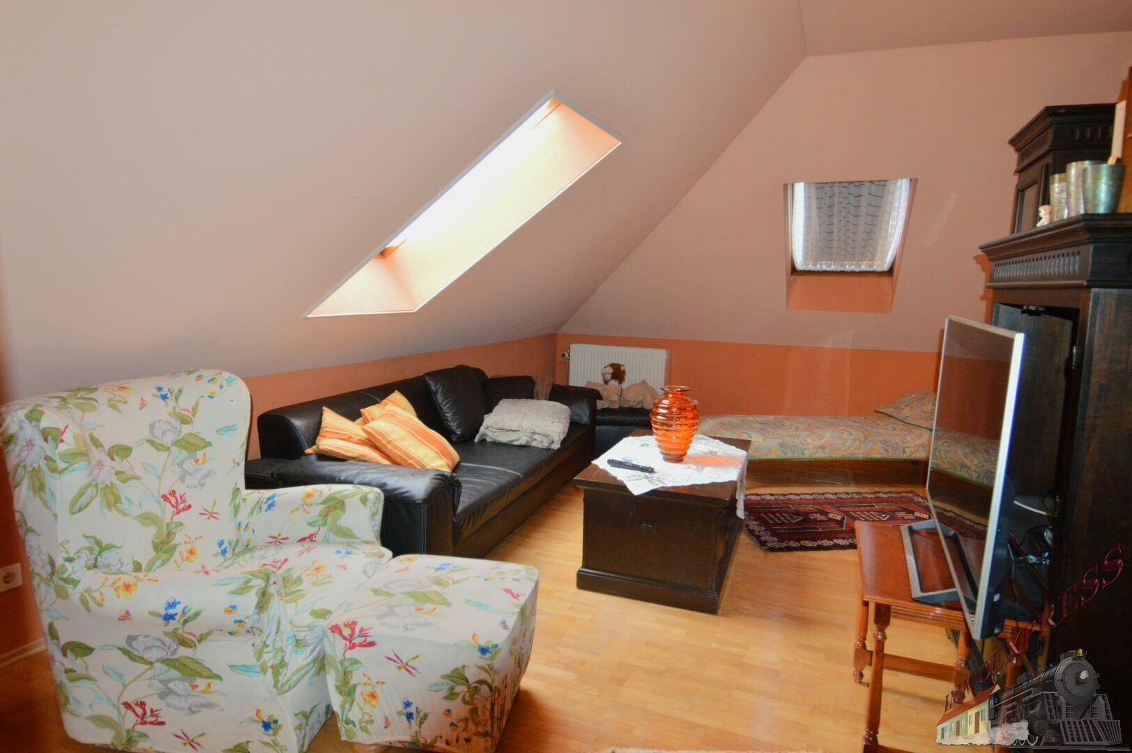 Dachgeschoss-Wohnbereich mit Sofa, Sessel und Dachfenstern für natürliches Licht.
