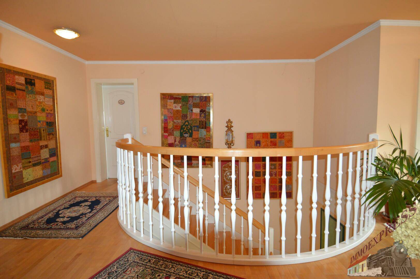Oberer Flur mit geschwungener Treppe, Holzboden und farbenfrohen Wanddekorationen.