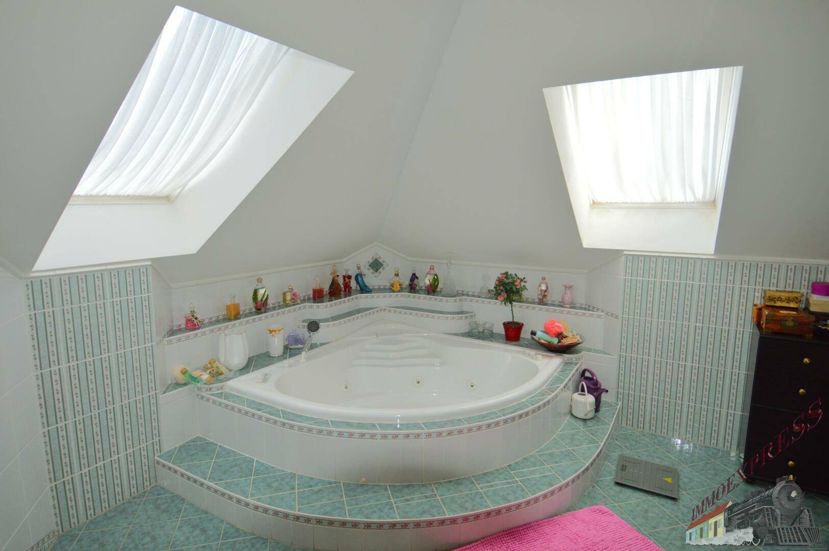 Eckbadewanne im Dachgeschoss-Badezimmer mit hellblauen Fliesen und zwei Dachfenstern.