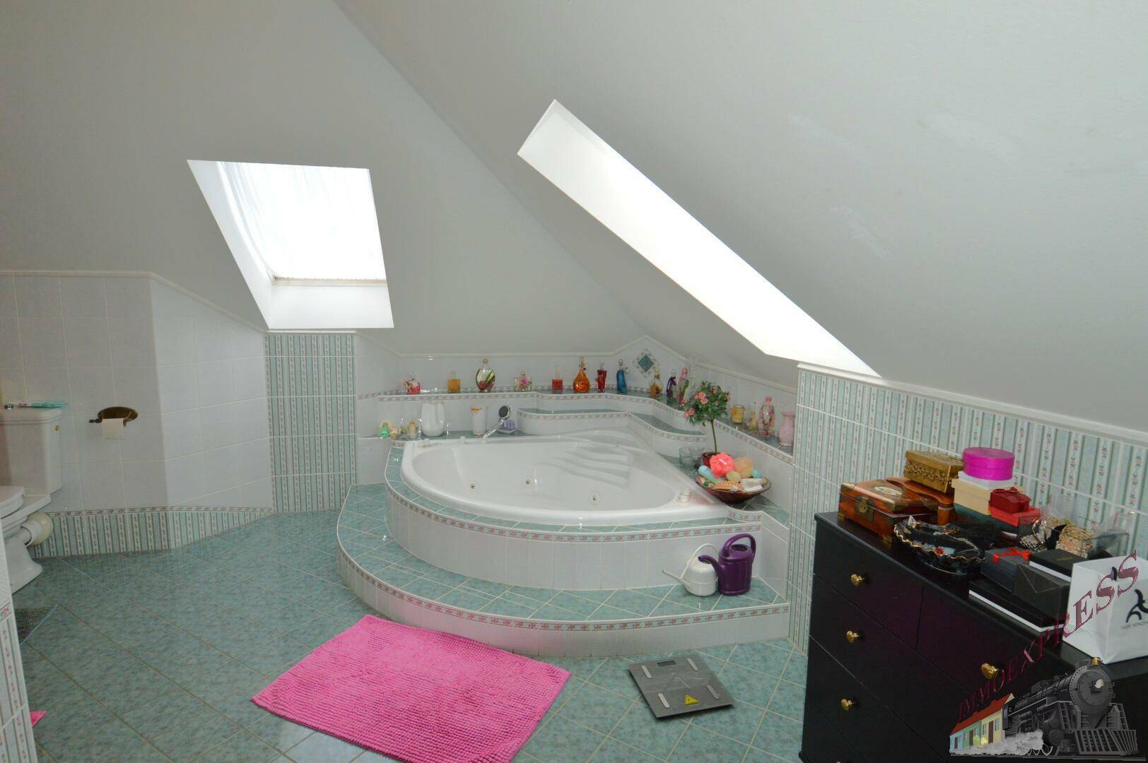 Geräumiges Badezimmer im Dachgeschoss mit Eckbadewanne, Dachfenstern und hellblauen Fliesen.