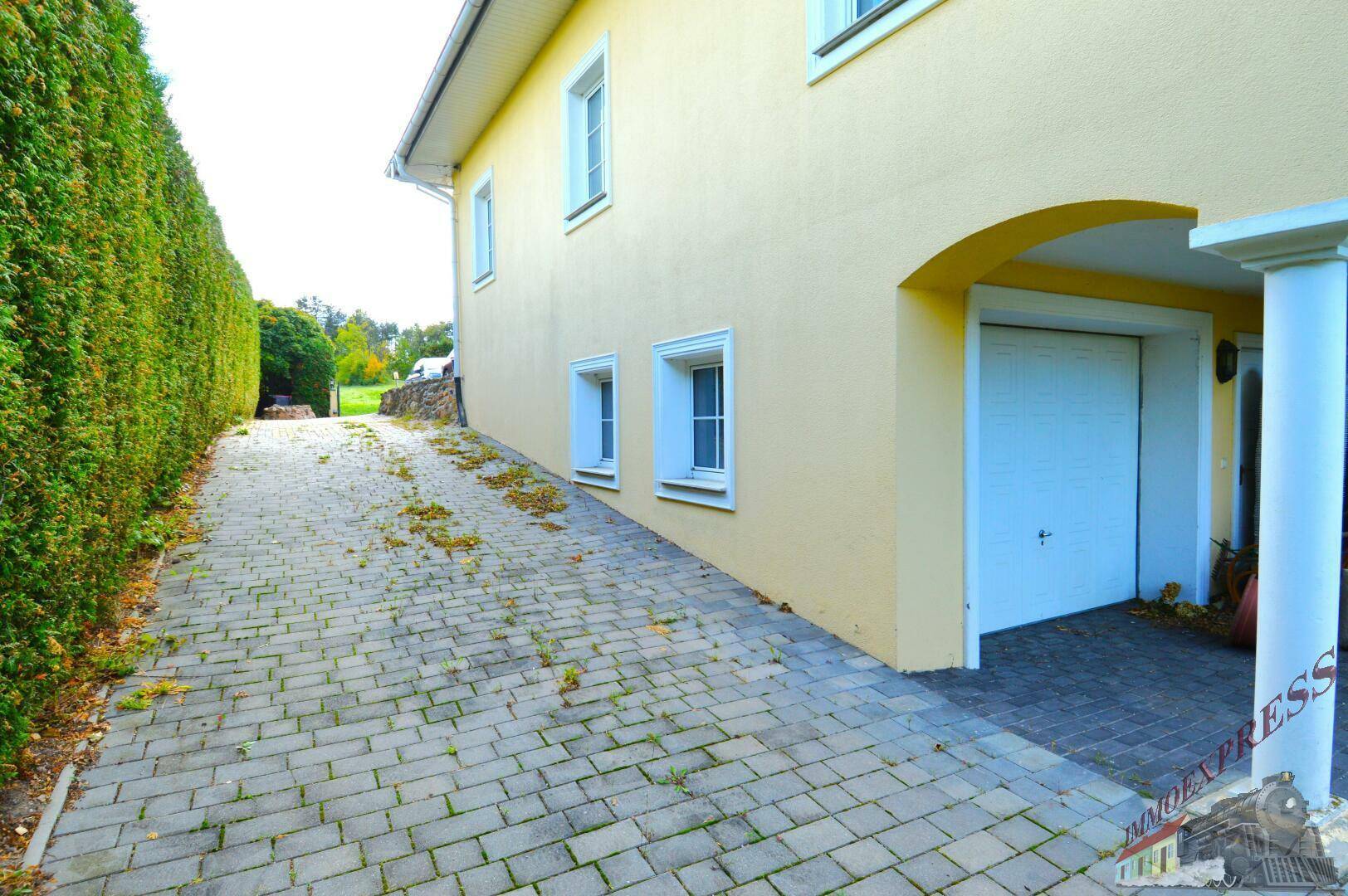 Gepflasterte Auffahrt zum Haus mit Garage und hoher Hecke.