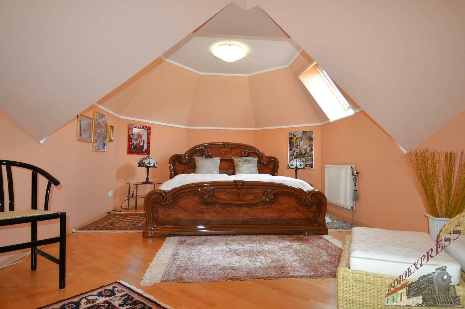 Geräumiges Schlafzimmer im Dachgeschoss mit kunstvollem Holzbett, Dachfenster und Teppichen.