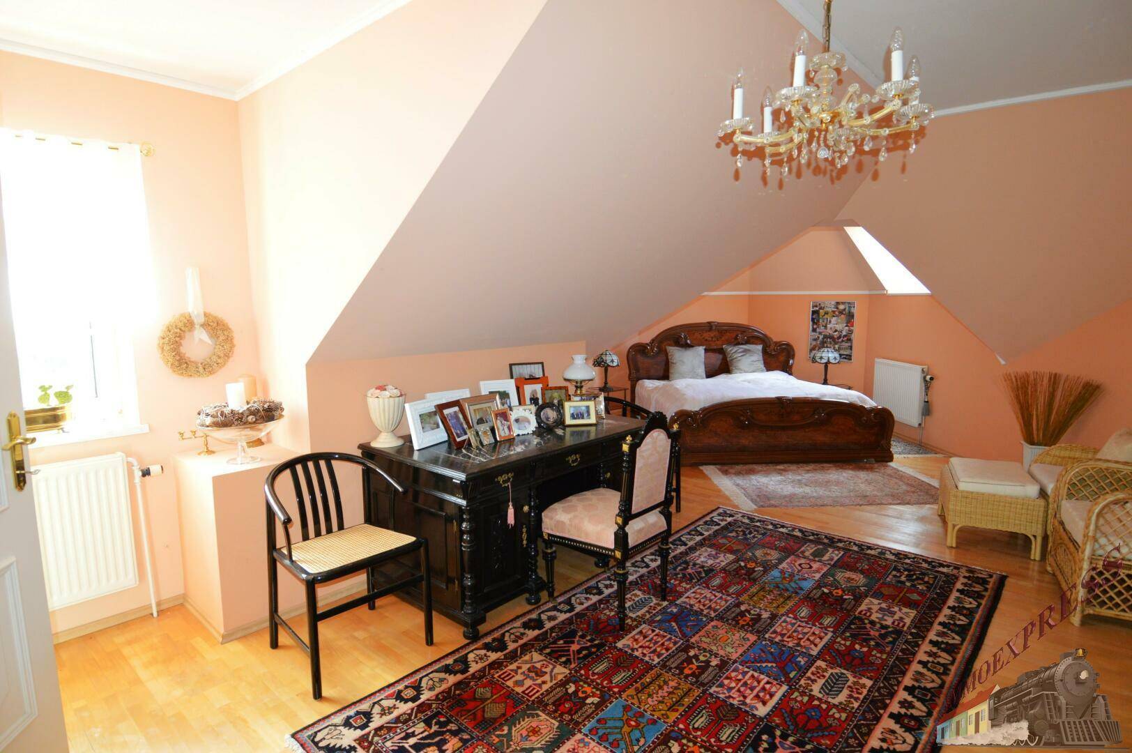 Schlafzimmer im Dachgeschoss mit großem Holzbett, Schreibtisch und Dachschrägen.