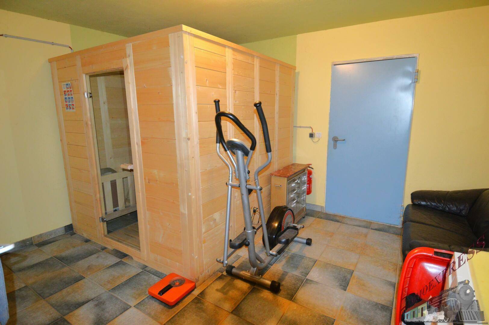 Fitnessraum im Keller mit Sauna, Trainingsgerät und Fliesenboden.