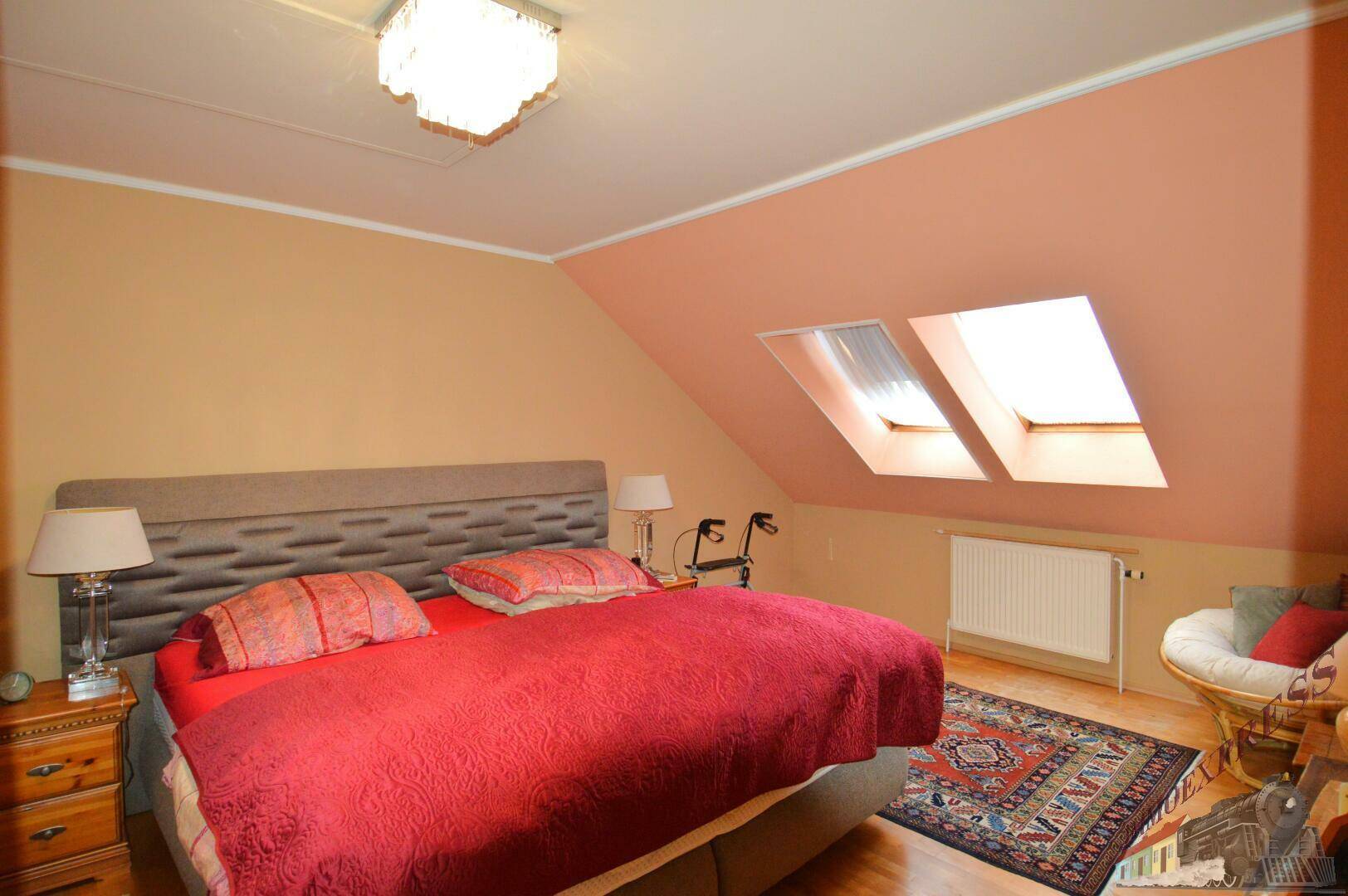Schlafzimmer im Dachgeschoss mit Doppelbett, Dachfenstern und warmen Farbtönen.