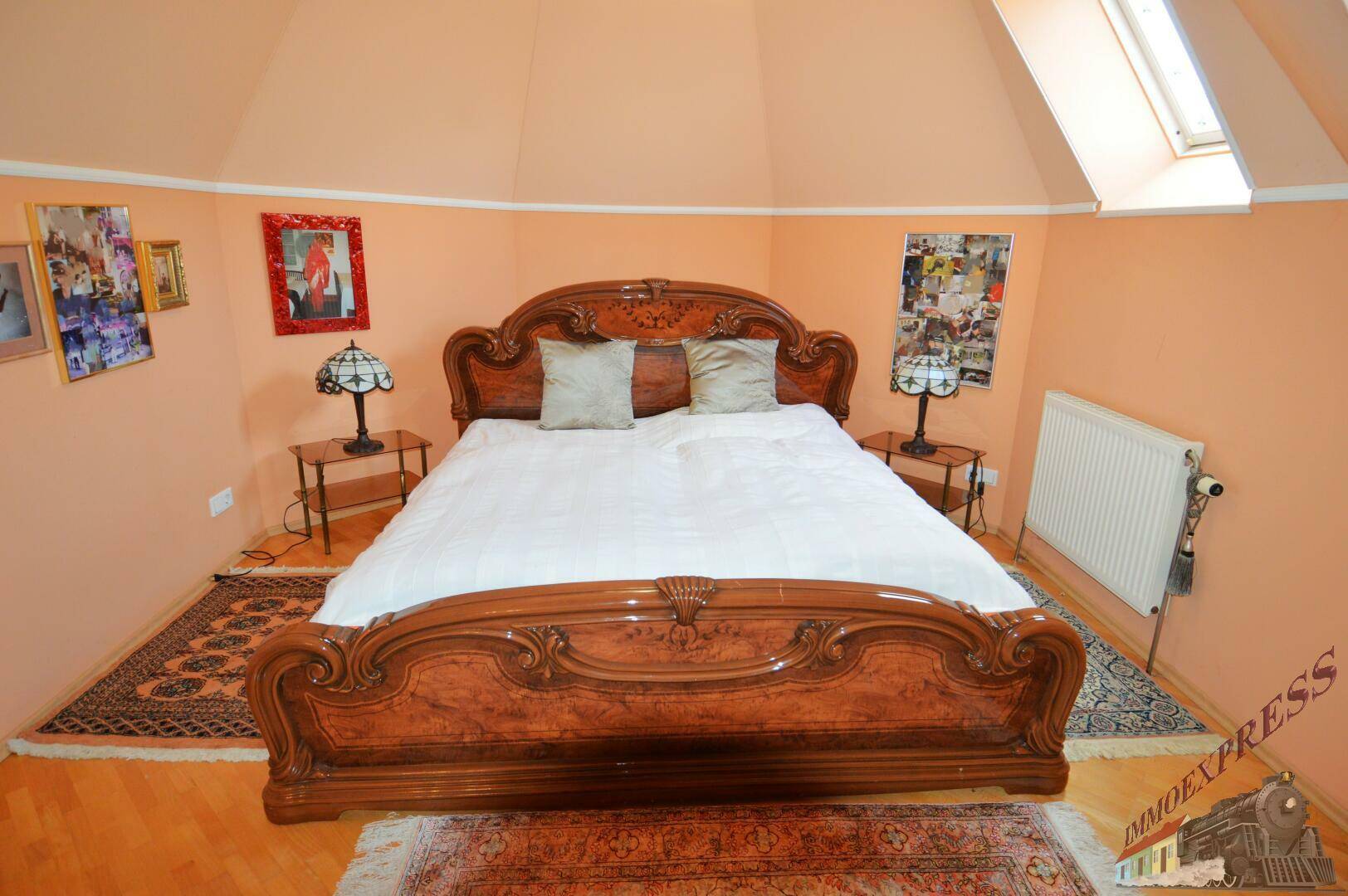 Detailansicht des kunstvollen Holzbettes im Dachgeschoss-Schlafzimmer mit traditionellen Teppichen.