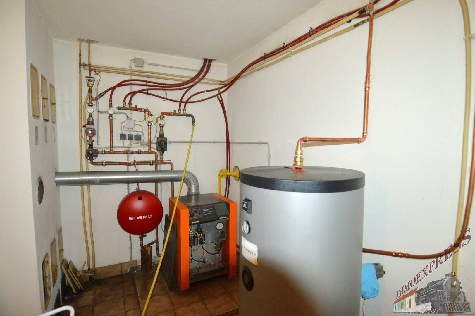 Heizungsraum mit Warmwasserspeicher, Heizkessel und sichtbaren Rohrleitungen.