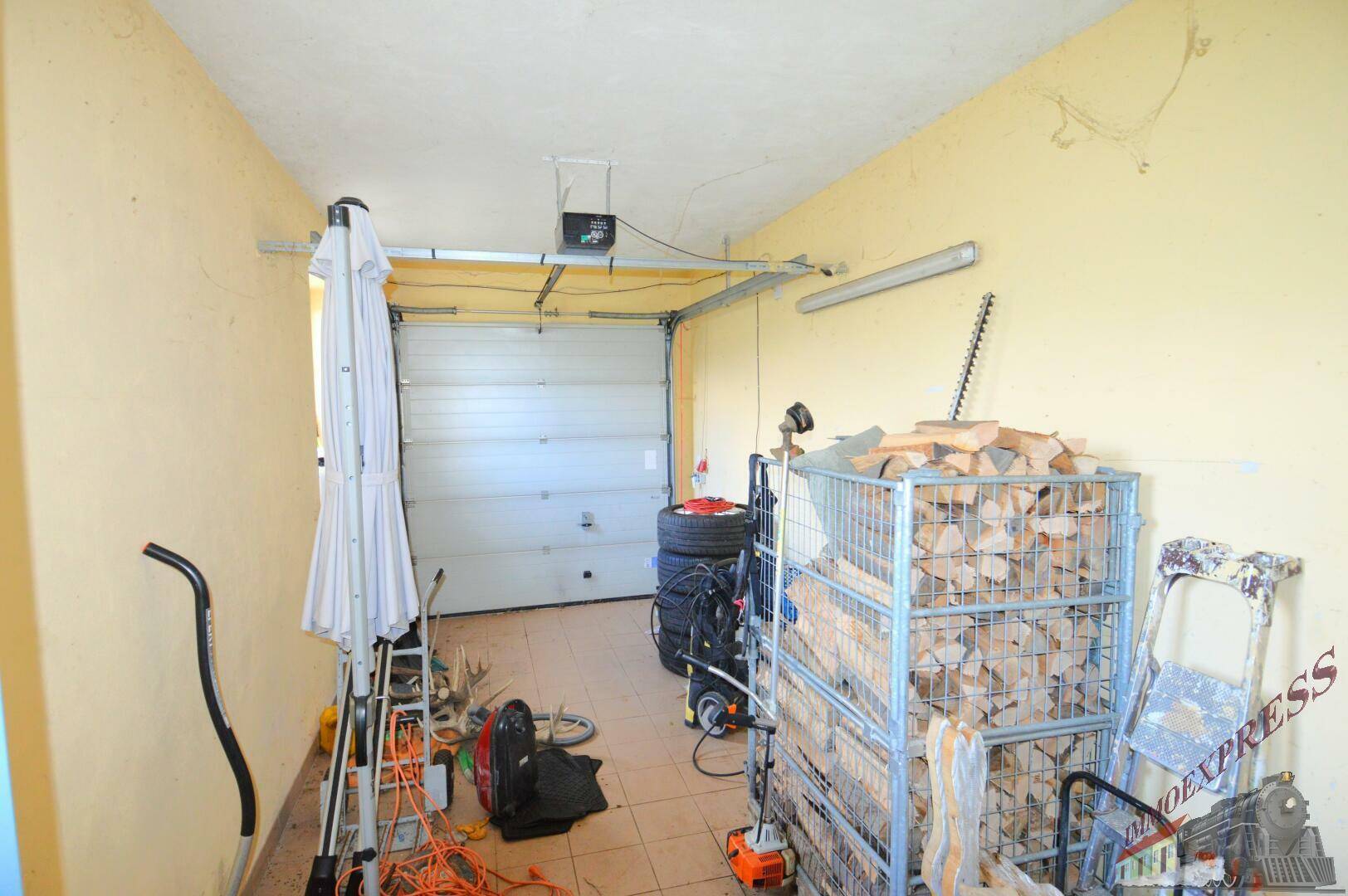 Garage mit Sektionaltor, gefliestem Boden und Lagerplatz für Holz.