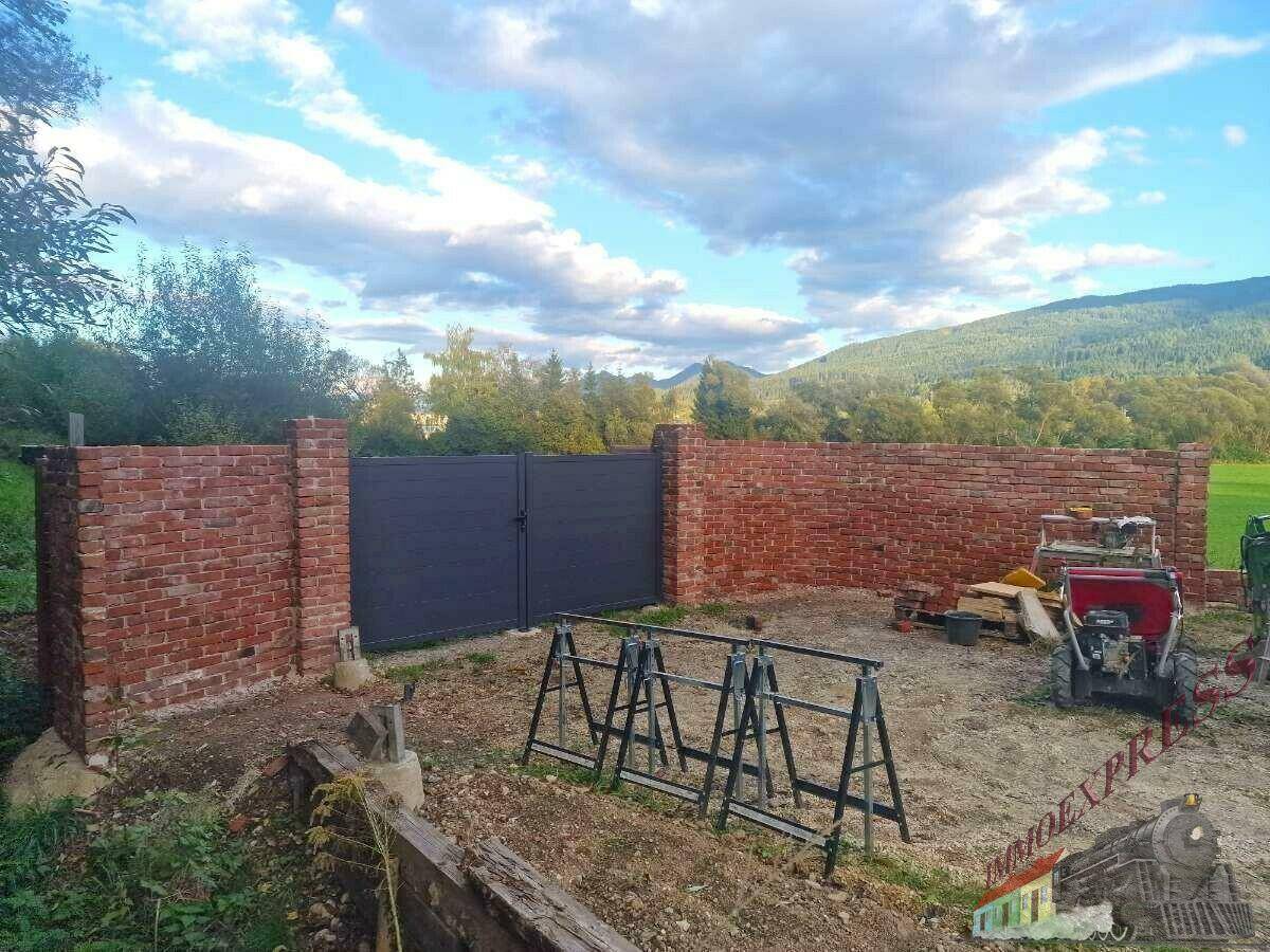Eine gemauerte Wand mit einem dunklen Tor und Blick auf die umliegende Landschaft und Berge.