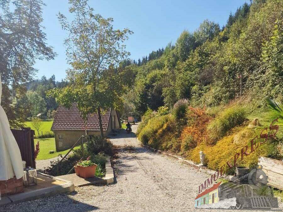 Eine Kiesauffahrt führt zu einem kleinen Gebäude, umgeben von üppiger grüner Vegetation und Bäumen.