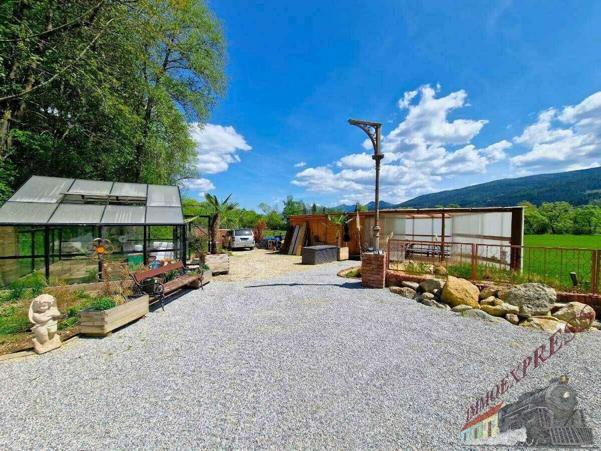 Großer Gartenbereich mit Gewächshaus, Sitzbank und weitem Blick in die Landschaft.