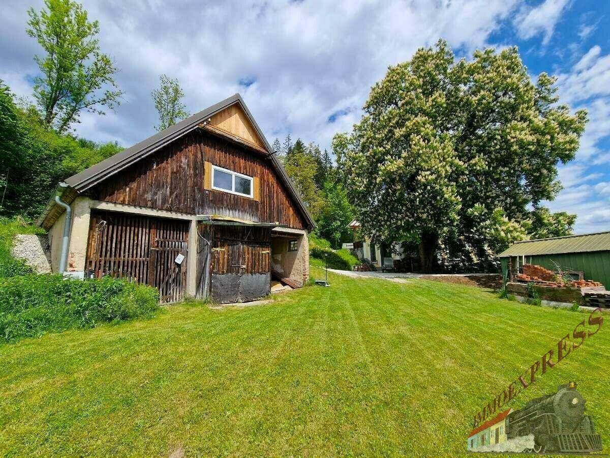 Rustikale Holzscheune auf einer weitläufigen grünen Rasenfläche mit einem großen Baum im Hintergrund.
