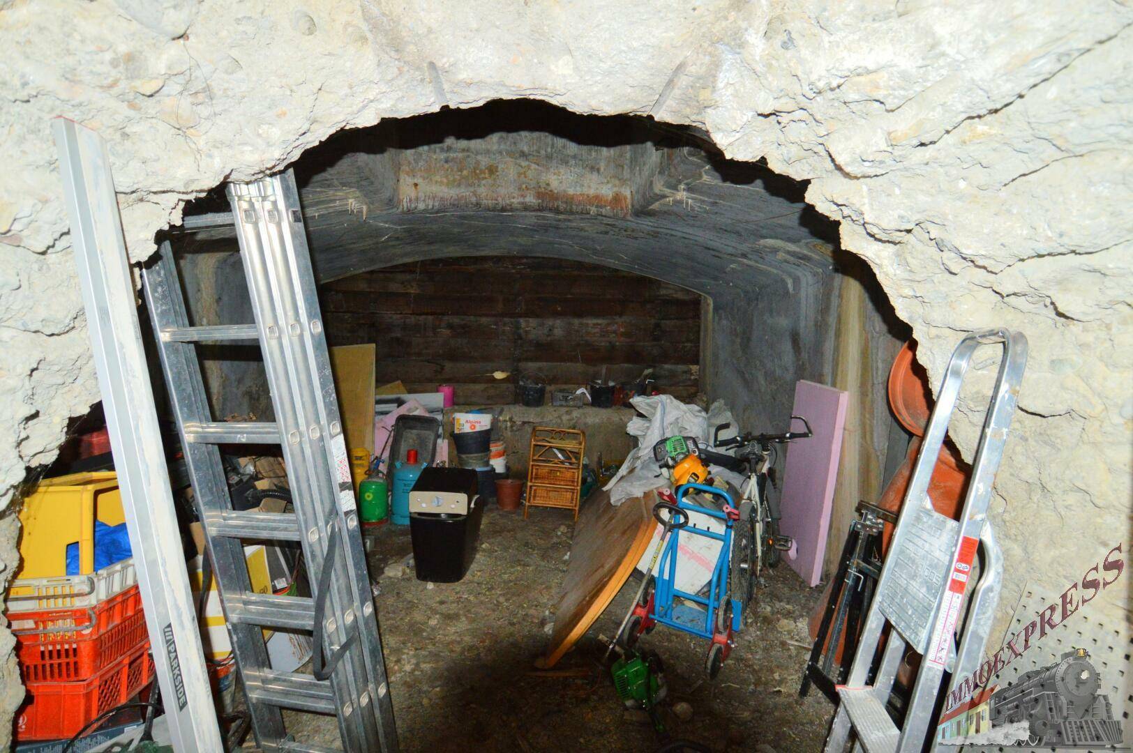 Eingangsbereich eines dunklen Kellerraums mit rauen Wänden und gelagerten Gegenständen.