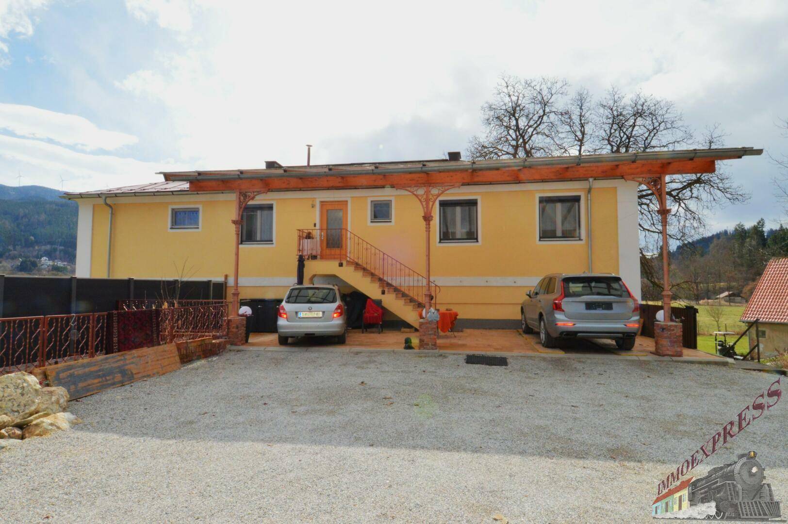 Vorderansicht des gelben Gebäudes mit überdachtem Carport und Außentreppe.