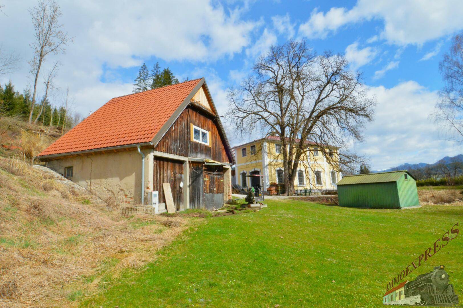 Rustikale Holzscheune und gelbes Gebäude auf einer weitläufigen grünen Rasenfläche.