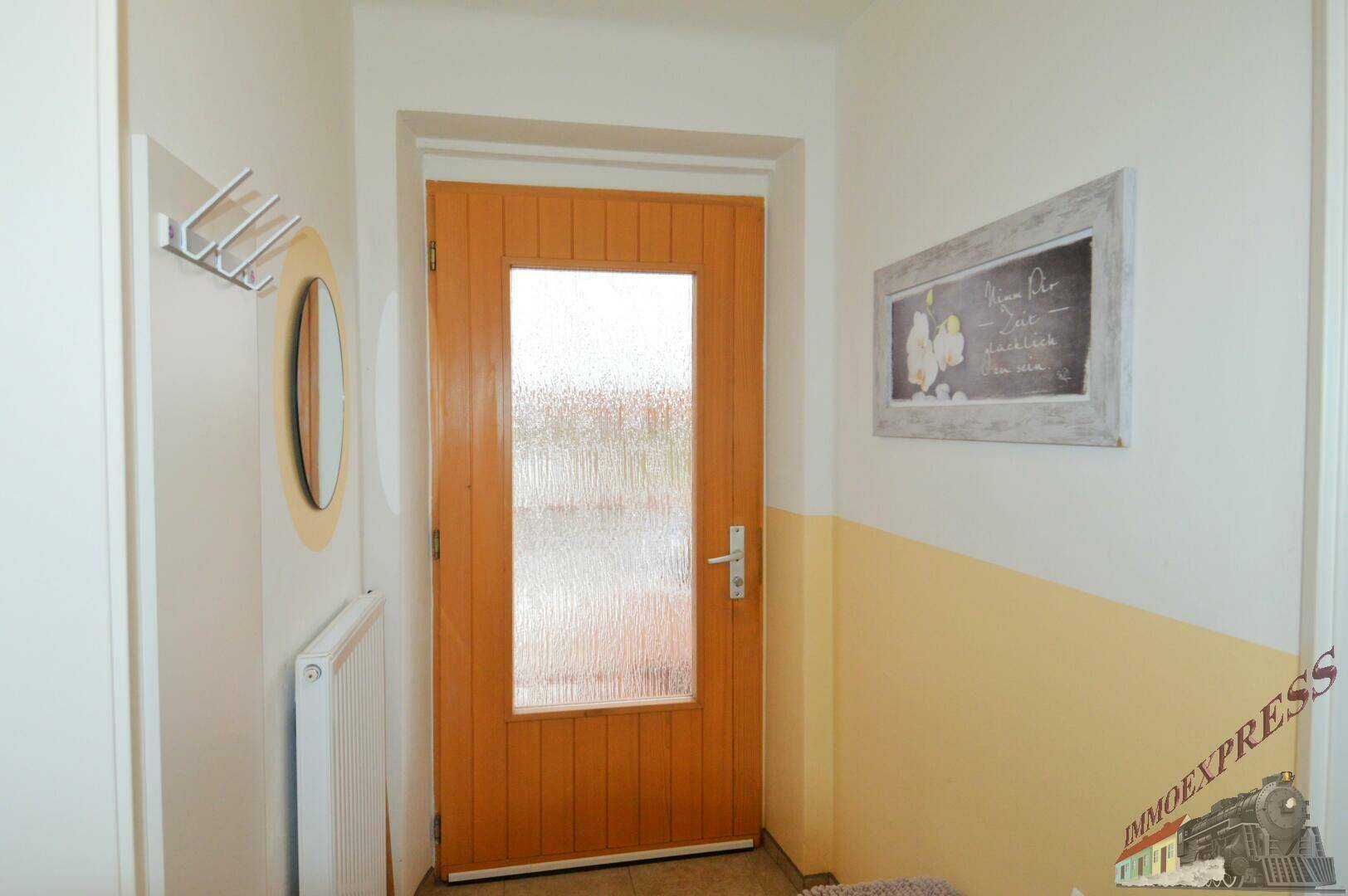 Heller Eingangsbereich mit Holztür, Garderobe und einem Spiegel an der Wand.