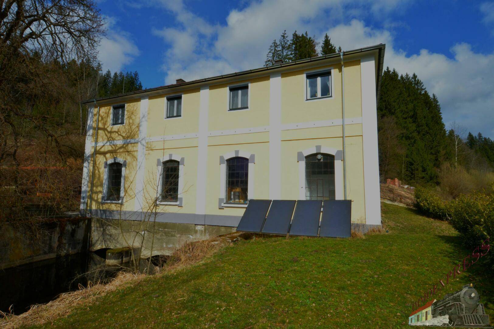 Seitenansicht des gelben Gebäudes mit Fenstern und Solarpaneelen auf dem Rasen.