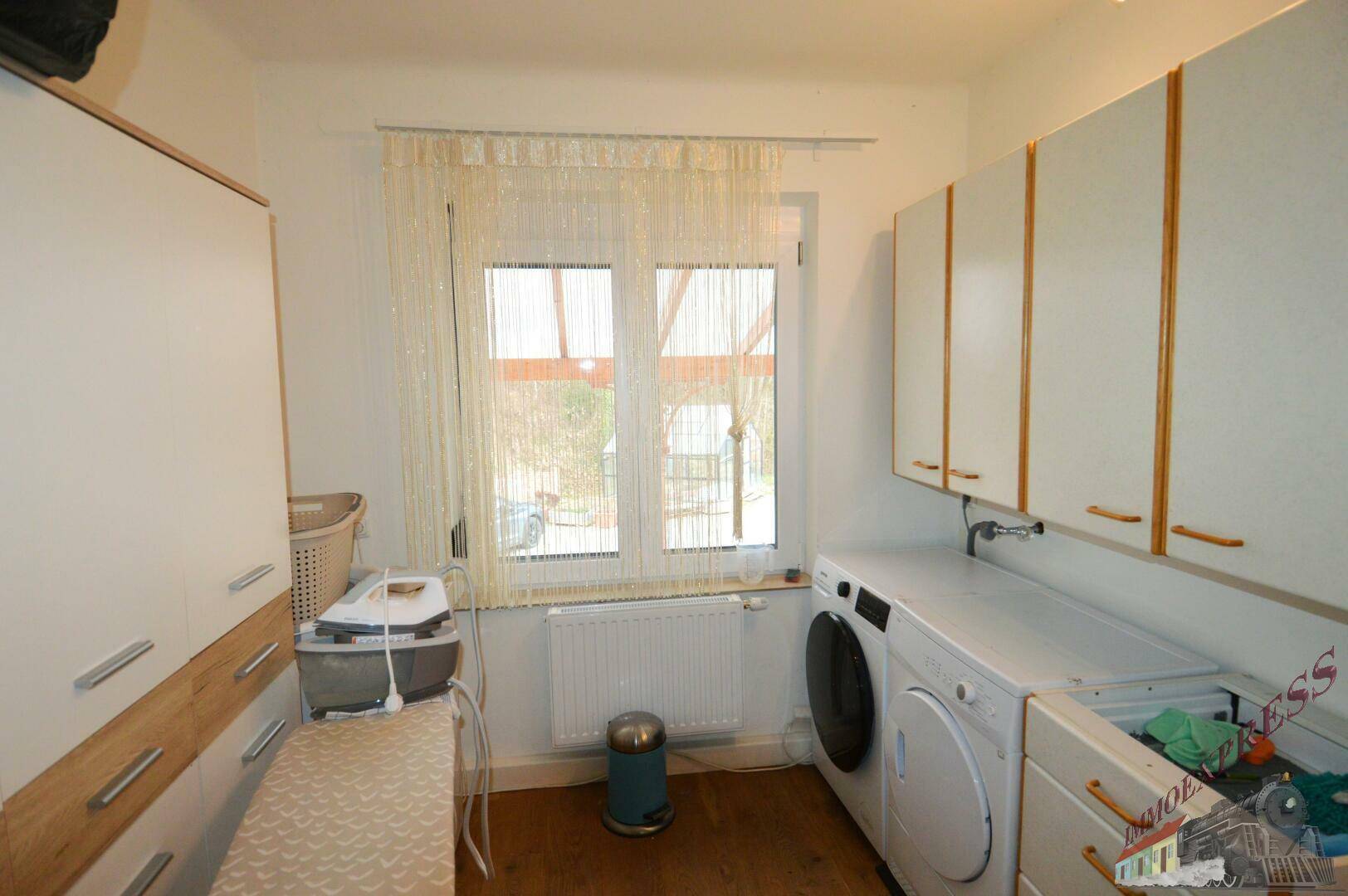Praktischer Hauswirtschaftsraum mit Waschmaschine, Trockner und Stauraum unter dem Fenster.