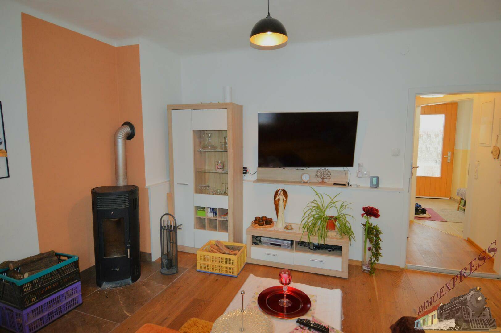 Wohnzimmer mit modernem Holzofen, Fernseher und gemütlicher Sitzecke.