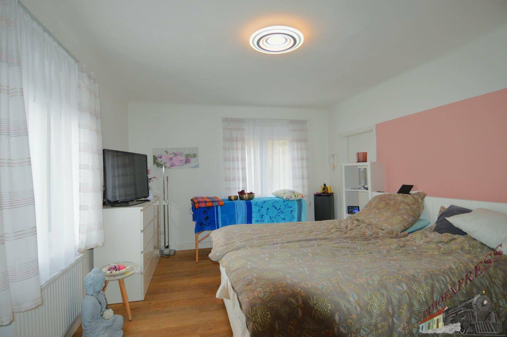 Schlafzimmer mit Doppelbett, Kommode und Fenster für natürliches Licht.