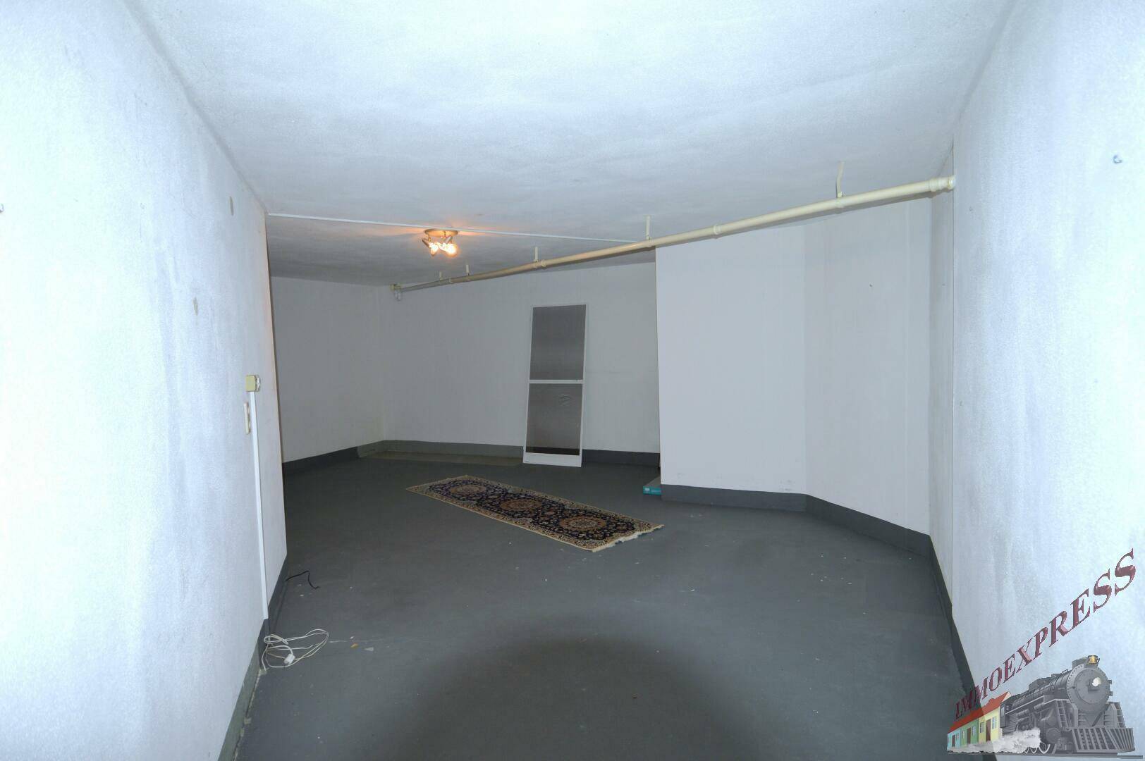 Großer, leerer Kellerraum mit Teppichläufer und kleinem Fenster.