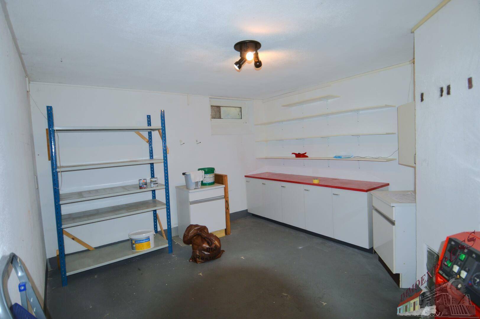 Kellerraum als Abstellfläche mit Regalen, Schränken und kleinem Fenster.