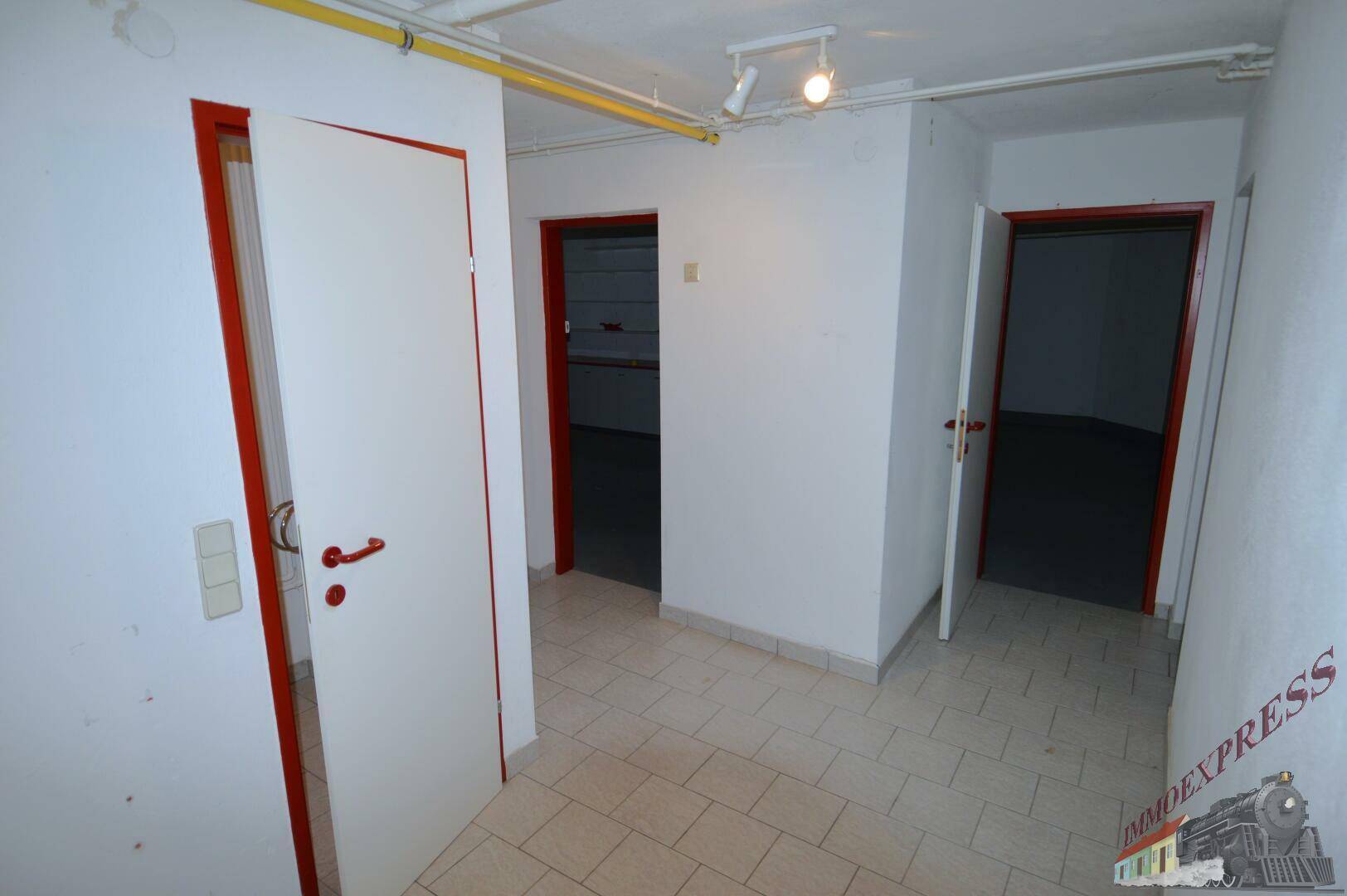 Kellerflur mit mehreren Türen, Fliesenboden und sichtbaren Leitungen an der Decke.