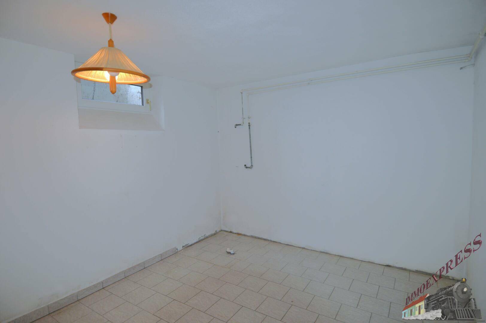 Kleiner Kellerraum mit Fenster und Fliesenboden, ideal als Abstellfläche.