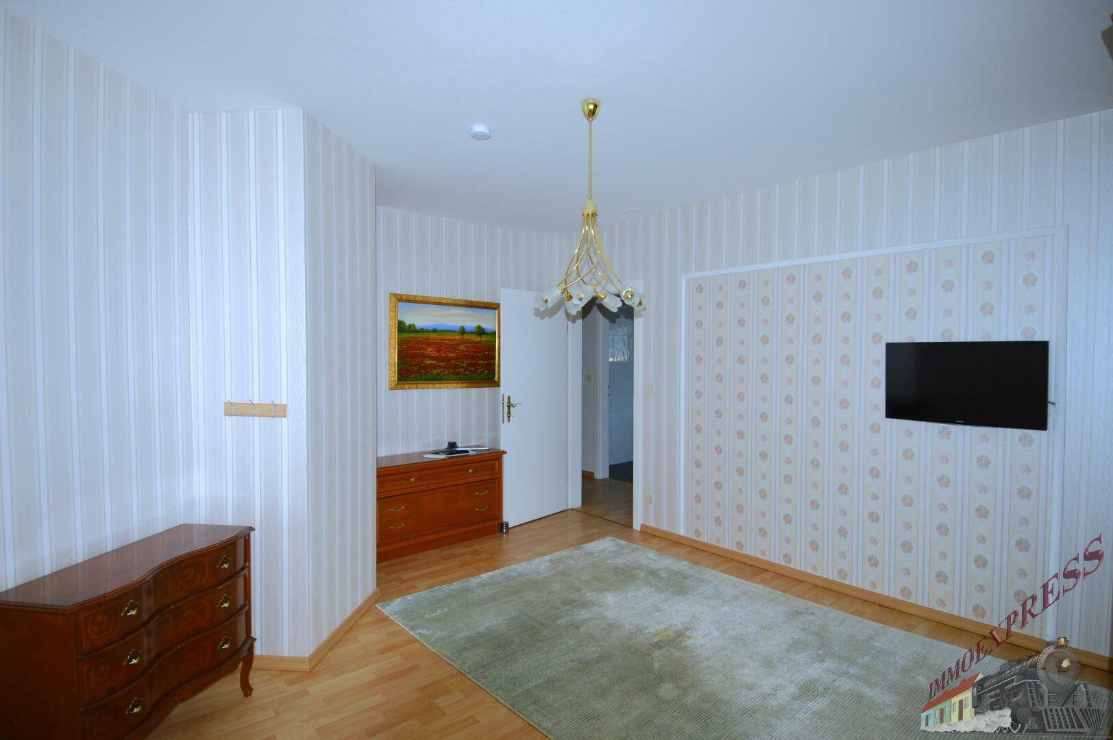 Schlafzimmer mit hellem Holzboden, gemusterten Tapeten und traditionellen Möbeln.