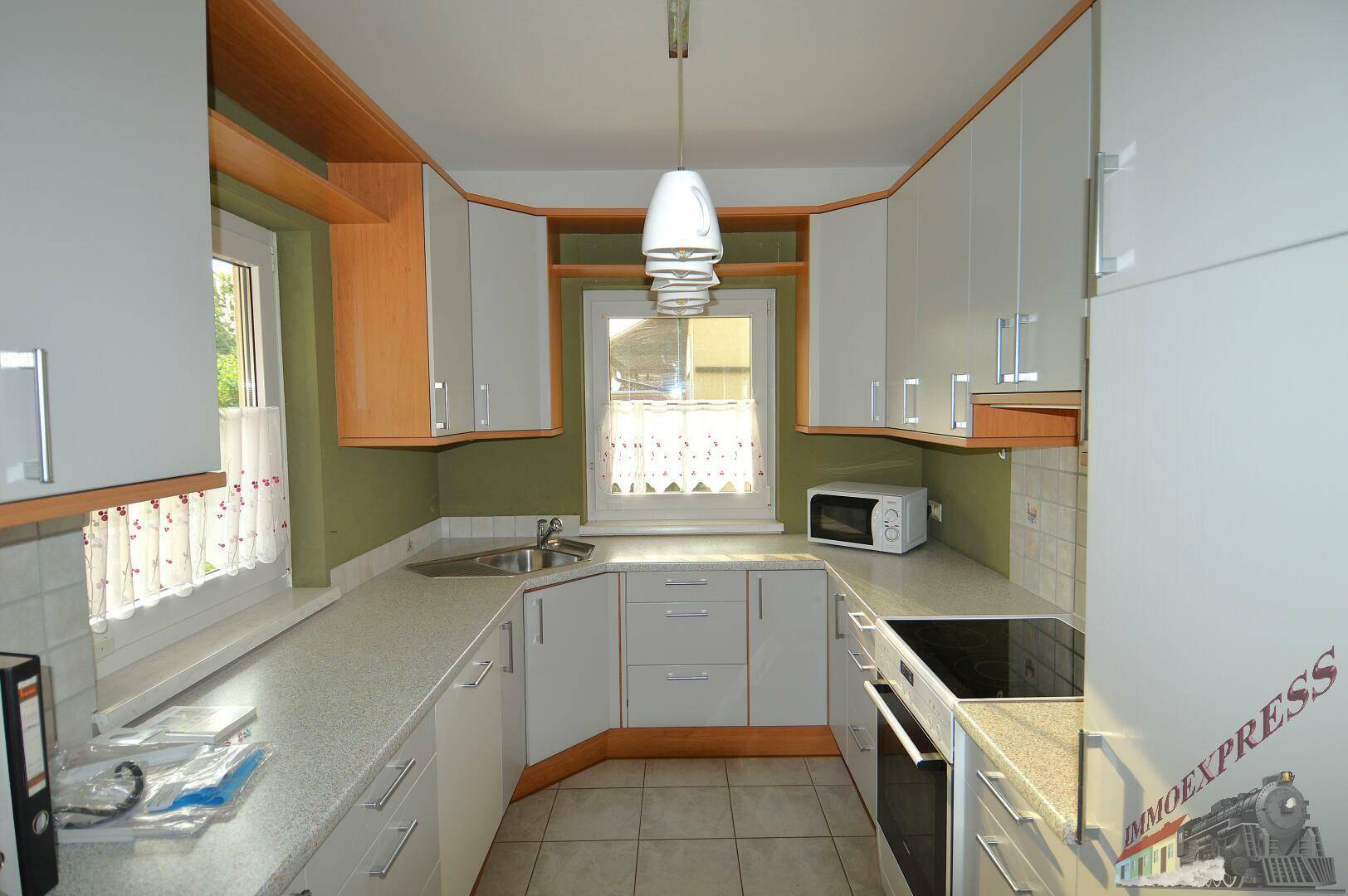 Funktionale Küche mit hellgrauen Schränken, Holzdetails und zwei Fenstern für Tageslicht.