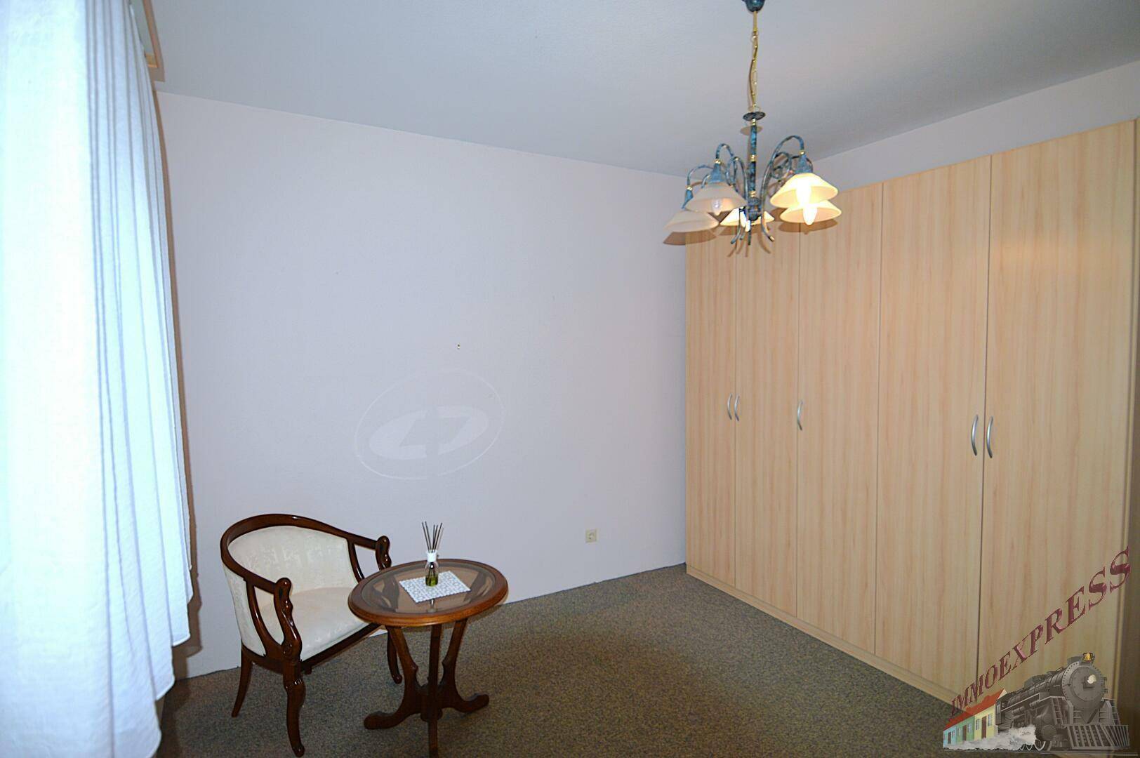 Helles Zimmer mit Teppichboden, großem Kleiderschrank und einem kleinen Beistelltisch.