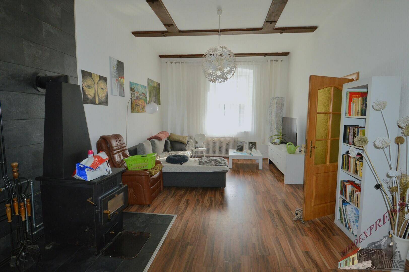 Geräumiges Wohnzimmer mit Holzbalken an der Decke, Kaminofen und Holzboden.