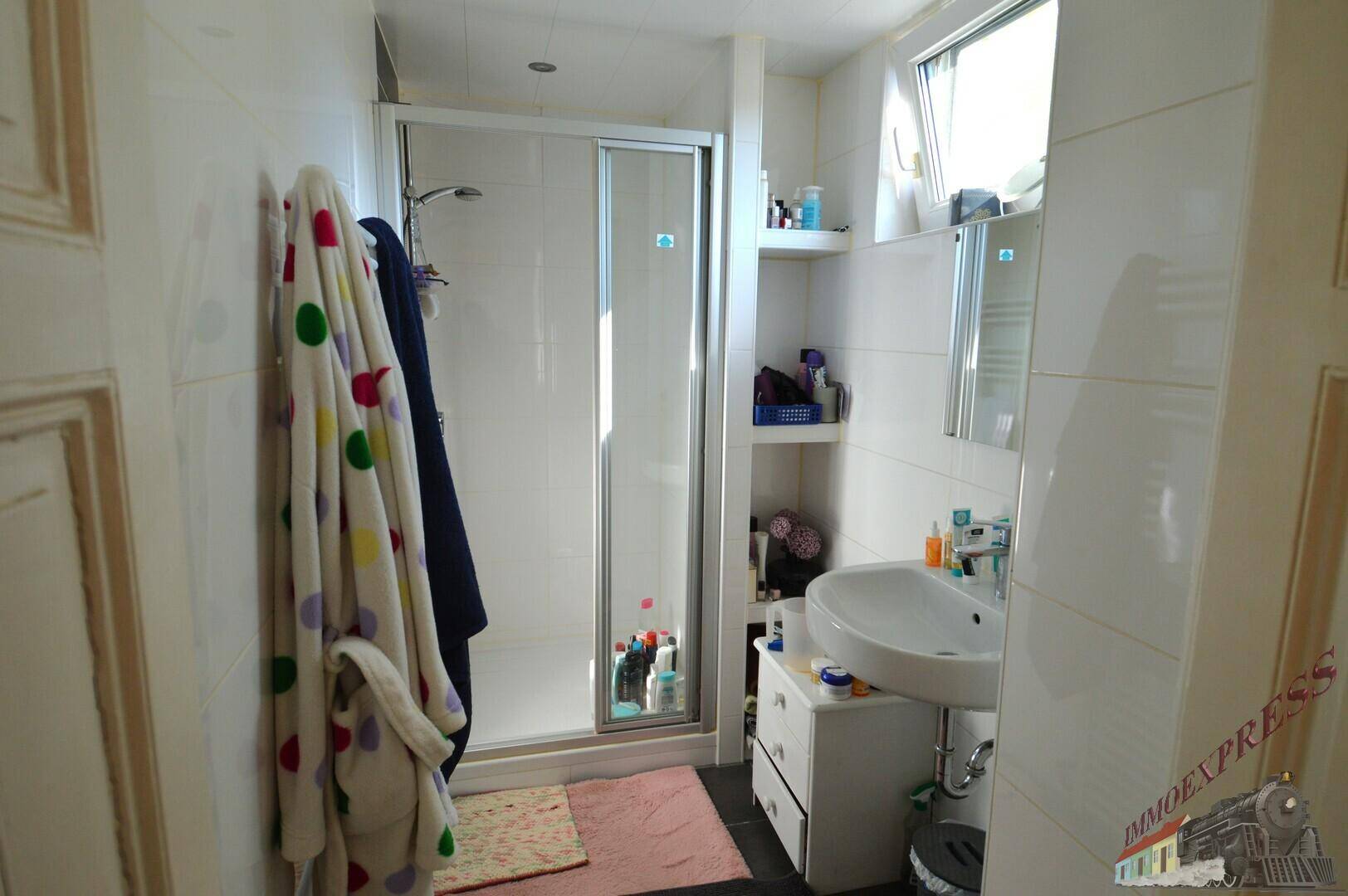 Helles Badezimmer mit Duschkabine, Waschbecken und einem Fenster für Tageslicht.