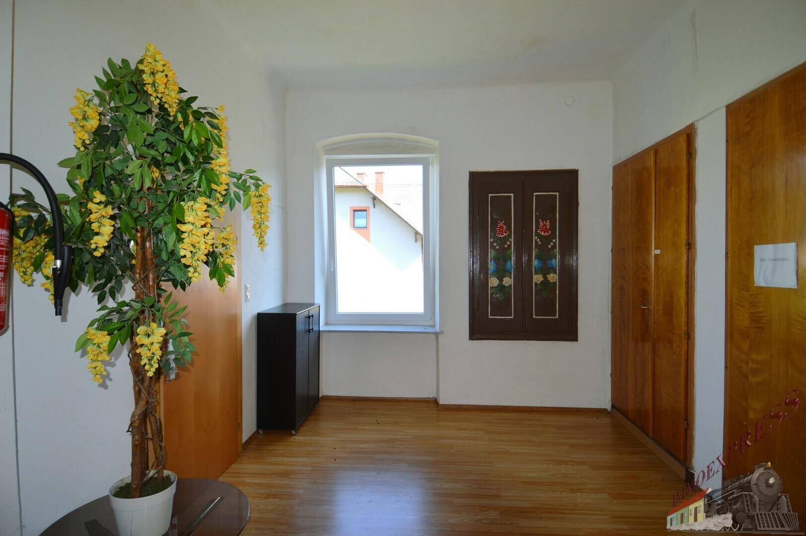 Heller Raum mit Holzboden, einem Fenster und Holzschränken an der Wand.