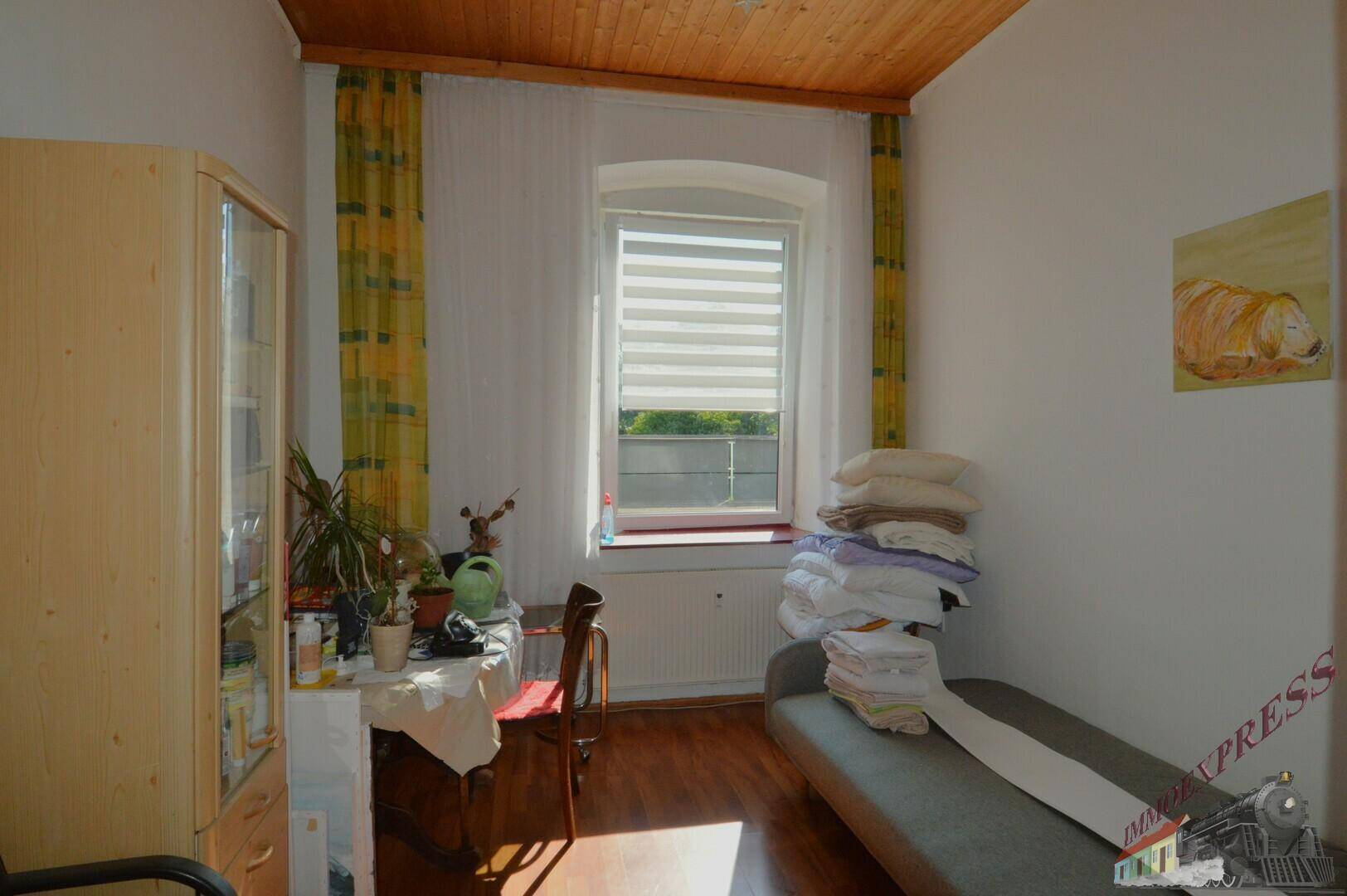 Helles Zimmer mit Holzdecke, Holzboden und einem Fenster mit Blick ins Grüne.
