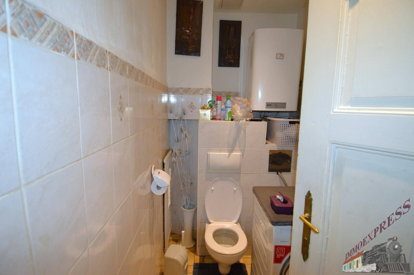 Kleines Gäste-WC mit weißen Fliesen, Toilette und einem Wandheizkessel.