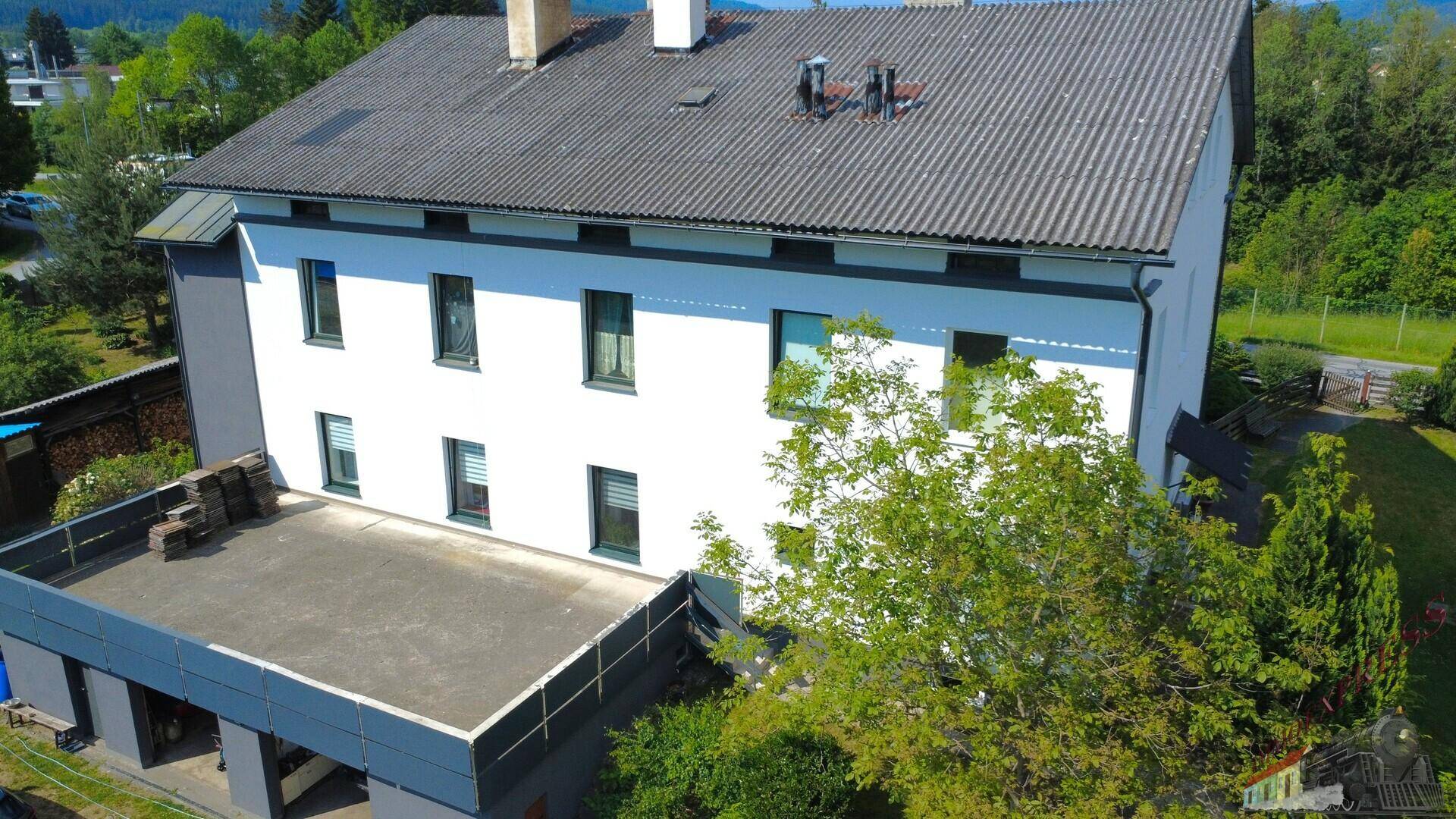 Rückansicht des Gebäudes mit einer großen, flachen Dachterrasse und angrenzendem Gartenbereich.
