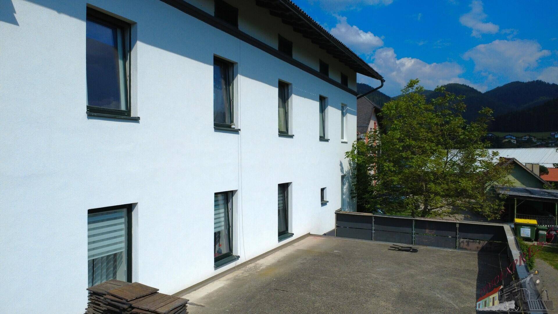 Detailansicht der Gebäudeseite mit Fenstern und der angrenzenden, ungenutzten Dachterrasse.