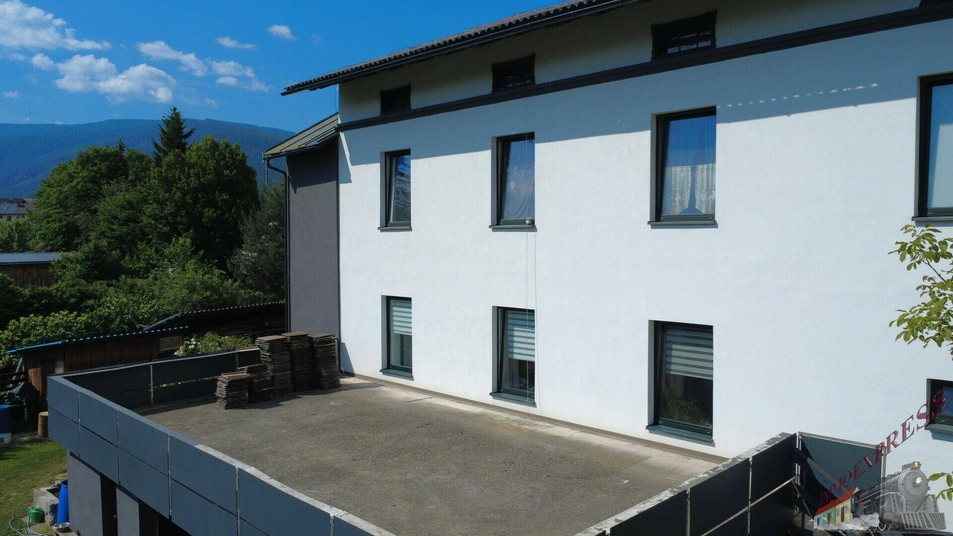Nahaufnahme der Gebäudefassade mit Fenstern und einer großen, unmöblierten Dachterrasse.