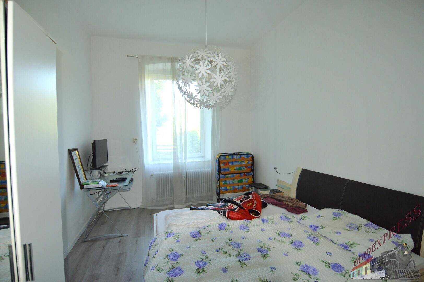 Schlafzimmer mit Bett, Schrank und einem Fenster, das viel Tageslicht hereinlässt.