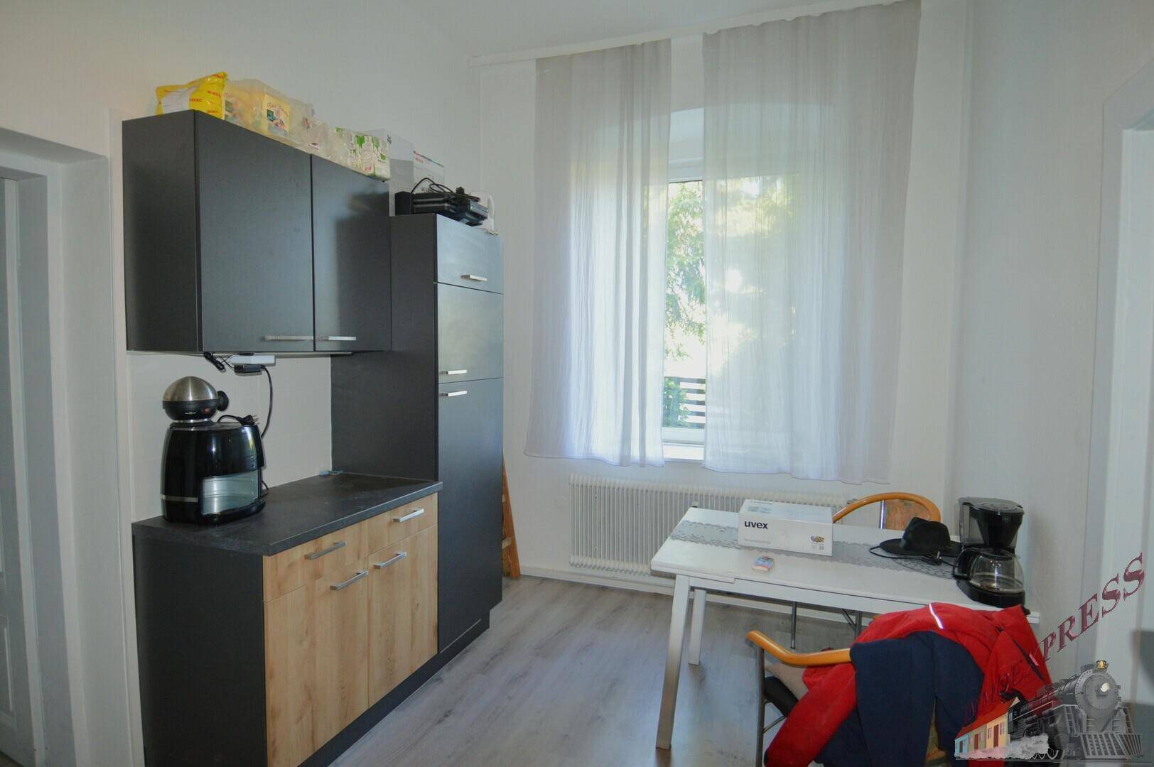 Moderne Küche mit grauen und holzfarbenen Schränken, Esstisch und Fenster.
