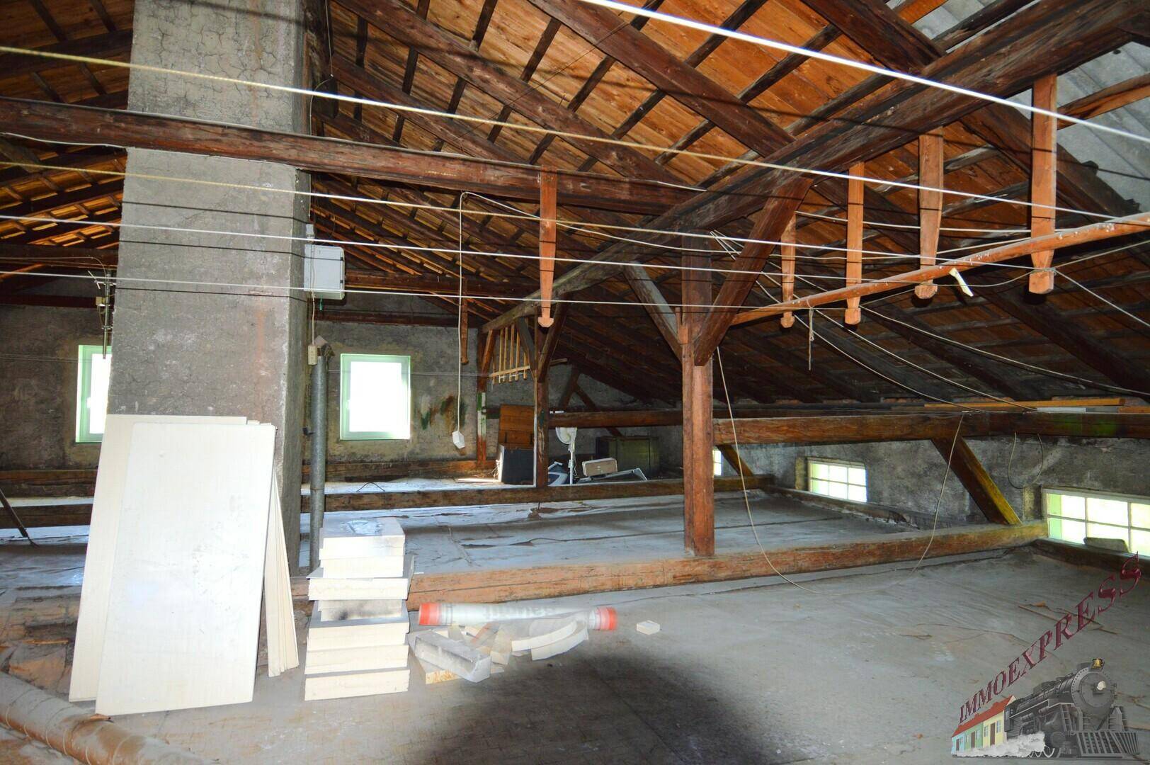 Geräumiger Dachboden mit sichtbaren Holzbalken, Dachschrägen und kleinen Fenstern, bereit für den Ausbau.