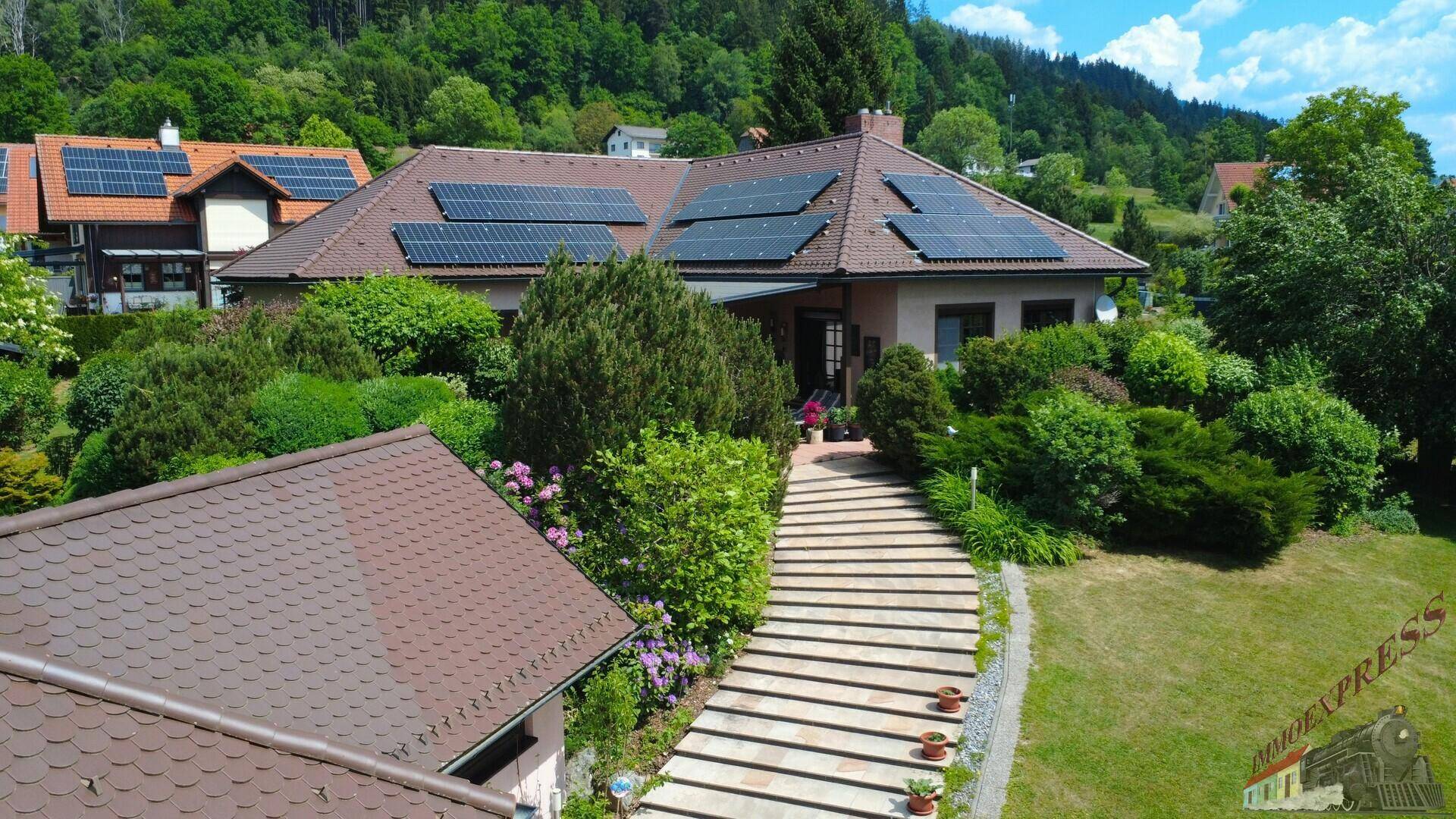 Luftaufnahme eines Hauses mit Solaranlagen auf dem Dach und einem gepflegten Gartenweg.