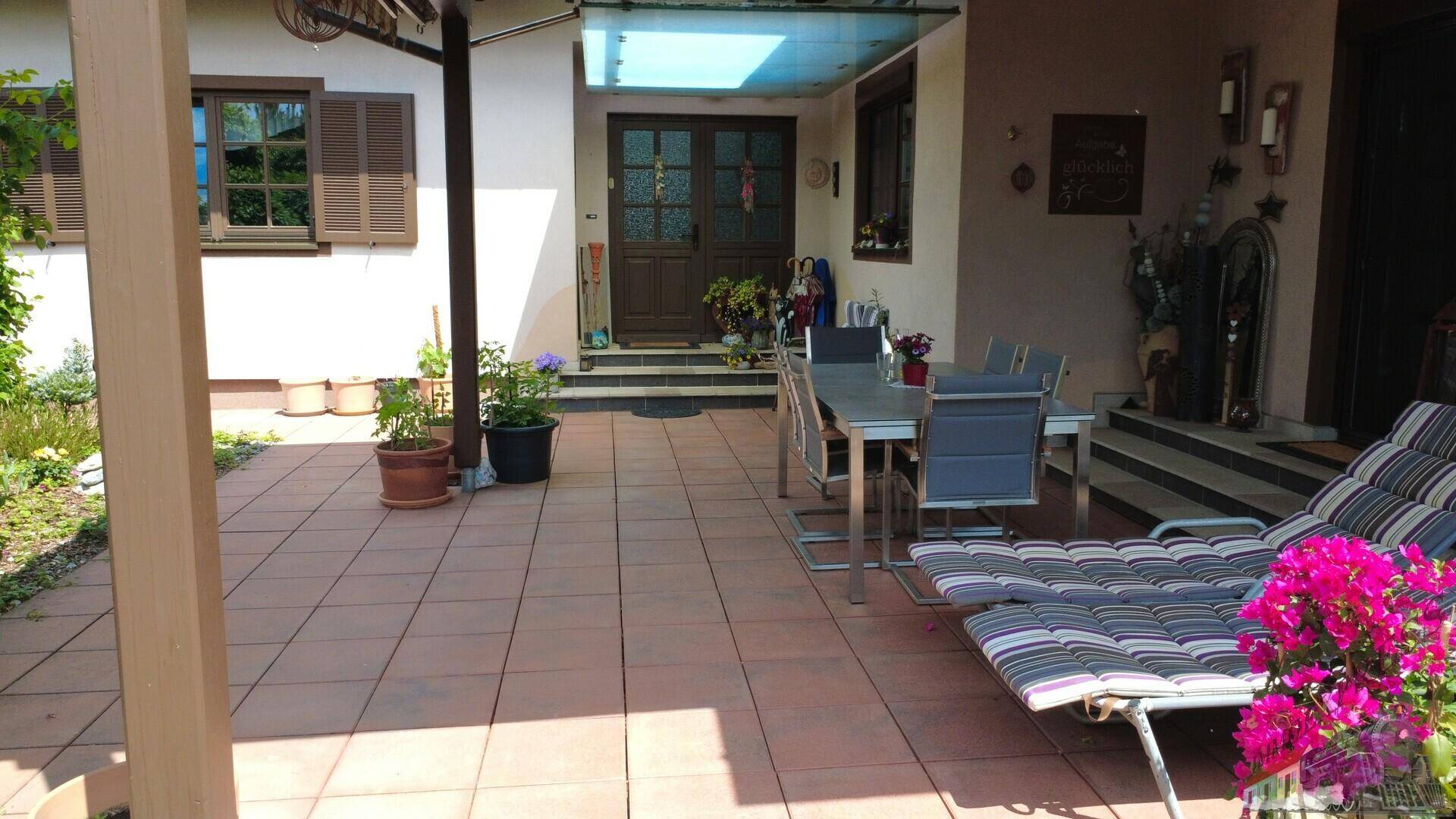 Große, geflieste Terrasse mit bequemen Liegestühlen und Zugang zum Haus.