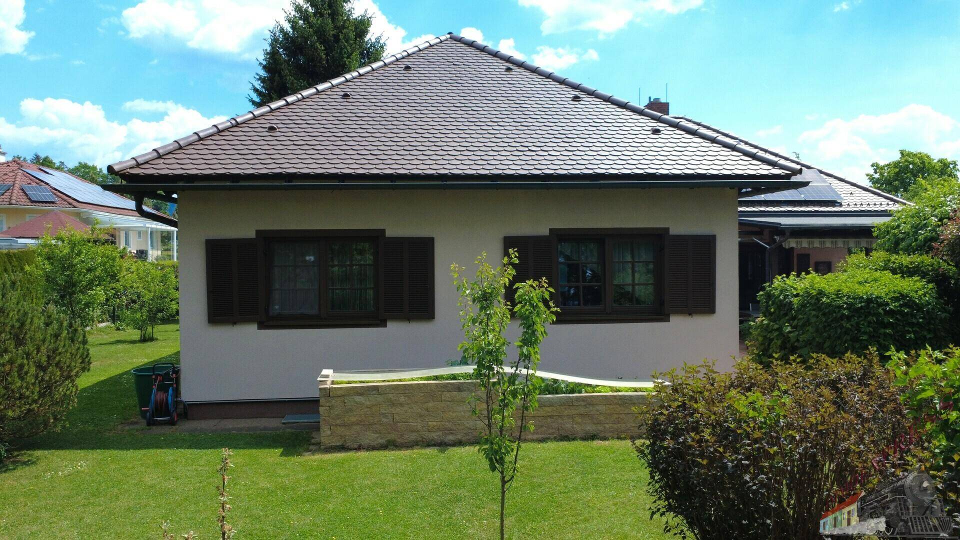 Seitenansicht des Hauses mit gepflegtem Rasen und Garten, umgeben von viel Grün.